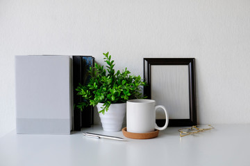 Workspace coffee mug, photo frame, plant and book on office table.