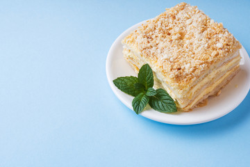 Layer cake with cream Napoleon millefeuille vanilla slice with mint on a colored blue background.