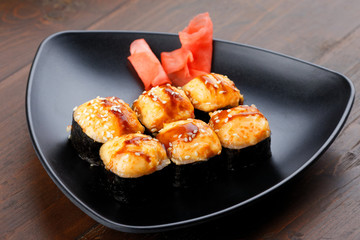 Appetizing baked hot sushi rolls. Set sushi on a black plate with ginger.