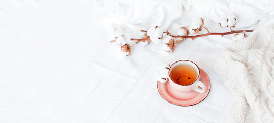 Cup of hot tea, branch of delicate cotton and knitted plaid sweater in bed with white linens. Cozy morning breakfast at home. Lifestyle gentle female background Copy Space autumn winter concept