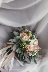 Stylish wedding bouquet of pink roses and green eucalyptus on background of sofa. Modern bride's bouquet on soft fabric in morning light. Wedding arrangements and decor