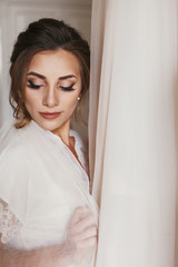 Gorgeous bride in silk robe holding stylish wedding dress in room in the morning. Happy sexy Bride and her beautiful wedding gown. Woman getting ready. Space for text