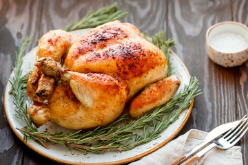 Whole grill chicken with caramelized skin and fresh rosemary on a wooden dinner table.