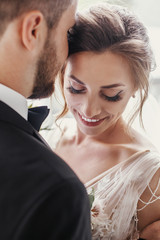 Gorgeous bride and stylish groom gently hugging and embracing at window light. Sensual wedding...