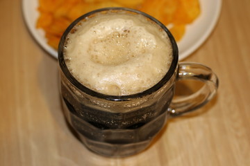 Foamy black beer and crispy chips on white plate