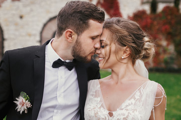 Gorgeous bride and stylish groom gently hugging and kissing outdoors. Sensual wedding couple...