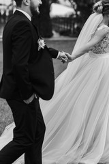 Gorgeous bride and stylish groom holding hands and walking outdoors. Happy Sensual wedding couple...