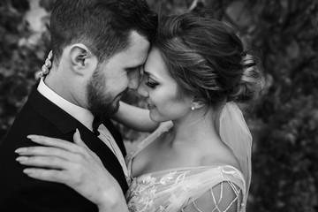 Gorgeous bride and stylish groom gently hugging and kissing outdoors. Sensual wedding couple...