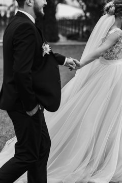 Gorgeous bride and stylish groom holding hands and walking outdoors. Happy Sensual wedding couple embracing. Romantic moments of newlyweds. Wedding photo