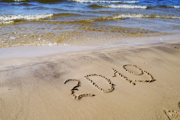 2019 written on the beach sand. Blue sea waves background. Concept for New year, Christmas greetings. Natural texture