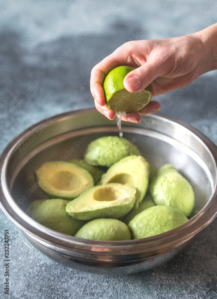 Wall mural hand squeezing lime on halved avocados