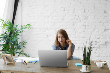Isolated shot of focused young woman working on creative start up project at home office, sitting in front of open portable computer against white brick wall background with copyspace for your text