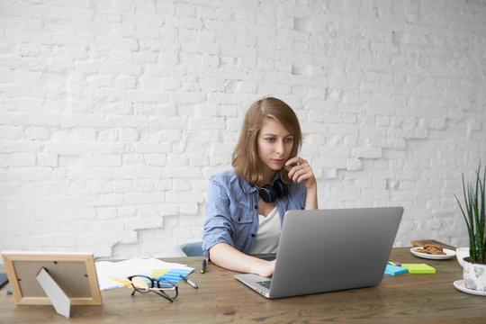 Job, occupation and electronic gadgets concept. Stylish young female working remotely on generic laptop, looking at screen with serious focused facial expression, absorbed with working process