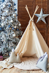 Christmas tree with gifts and wigwam in child room, copy space. Childen room interior with decorated play tipi tent. Scandinavian style 