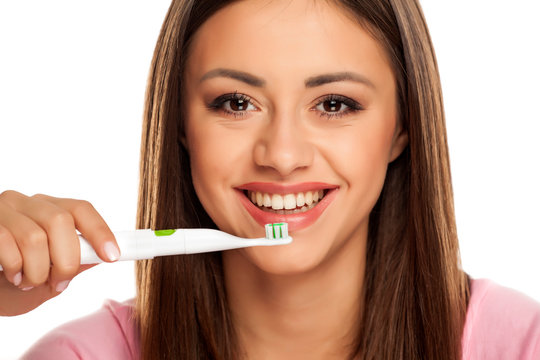 young woman brushing her teeth with electric tooth brush on white background