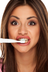 young woman brushing her teeth with electric tooth brush on white background