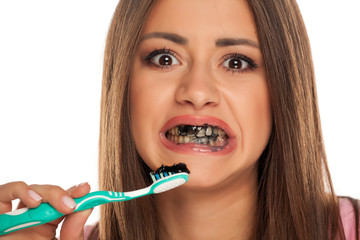 young woman brushing her teeth with black active charcoal toothpaste on white background