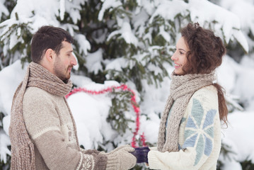 Happy young couple holding hands in winter park. Snowy concept. Couple in sweater and scarf.