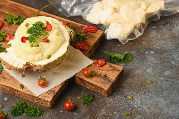Mashed celery root on wooden cutting board on dark background. Horizontal.
