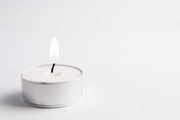 white tealight candle isolated in white, clean backgroung; with flame - obrazy, fototapety, plakaty
