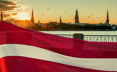 Conceptual collage image symbolizing 100 years of Latvian State Independence. Flag of Latvian State and background of mediaval historical center of Riga -capital of Latvia, EC - obrazy, fototapety, plakaty
