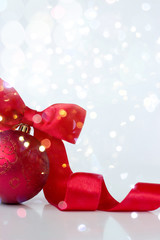 Red christmas ball, with red ribbon and bow, on white background with bokeh; christmas background