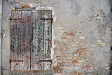 Old dirty wall with closed window with shutters. Aged italian street wall background with bricks and plaster, texture.