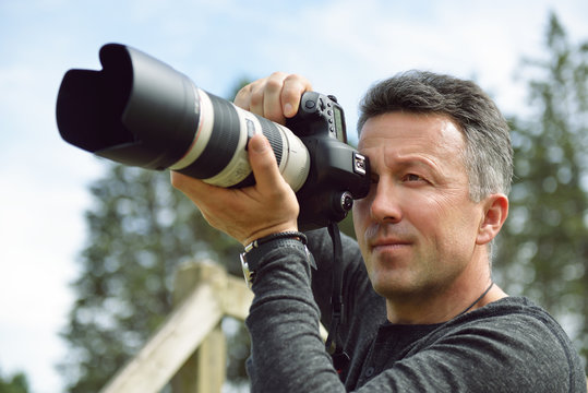 Man professional photographer with digital camera takes photos outdoor. Photo camera in male hands. Destination photographer at work. Paparazzi with telephoto lens