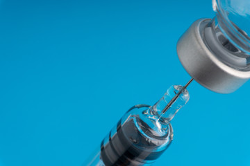 Medical syringe and vial on blue background with selective focus and crop fragment