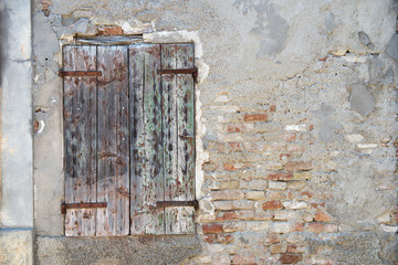 Old dirty wall with closed window with shutters. Aged italian street wall background with bricks and plaster, texture.
