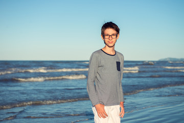 Young boy posing at the summer beach. Cute spectacled smiling happy 12 years old boy at seaside, looking at camera. Kid's outdoor portrait over seaside.