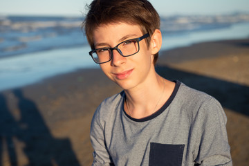 Young boy posing at the summer beach. Cute spectacled smiling happy 12 years old boy at seaside, looking at camera. Kid's outdoor portrait over seaside. © Khorzhevska
