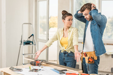 upset young couple standing near table with tools during house repair