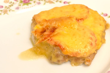 Baked meat with tomatoes and cheese on a white plate, close-up