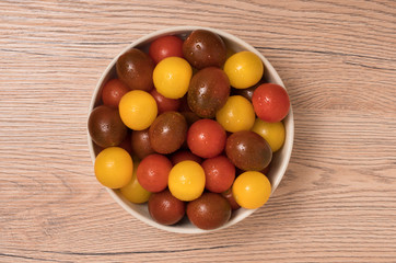 Cherry tomatoes, red,yellow and kamato in ceramic bowl on wooden background.