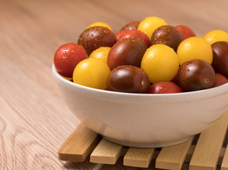 Cherry tomatoes in ceramic bowl on wooden background.