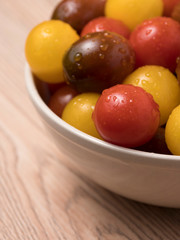 Cherry tomatoes in ceramic bowl on wooden background.