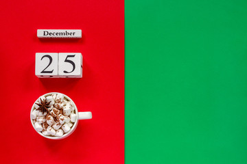 Wooden calendar December 25th and cup of cocoa with marshmallows on red and green background. Top view Flat lay Concept Christmas day Copy space