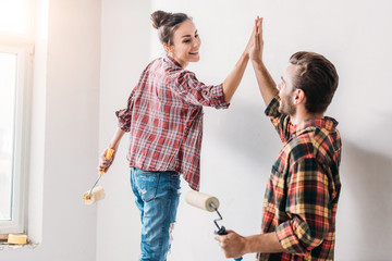 happy young couple giving high five while painting wall in new apartment