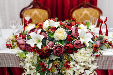 Wedding presidium in restaurant. Wedding banquet table for newlyweds with flowers, greenery. Lush floral arrangement on wedding table. Luxury wedding decorations