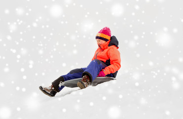 Fototapeta na wymiar childhood, sledging and season concept - happy little girl sliding down on sled outdoors in winter