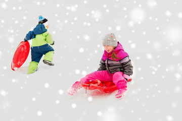 childhood, sledging and season concept - happy little kids sliding on sleds down snow hill in winter