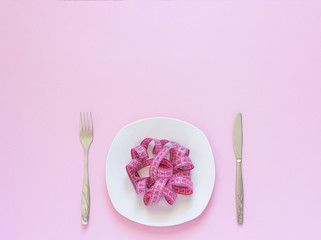Pink measuring tape lying on plate in the form of spaghetti, knife and fork on pink background. Diet or anorexia concept. Top view Copy space - obrazy, fototapety, plakaty