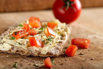 Crispbread with cheese cream, tomatoes pieces and herbs