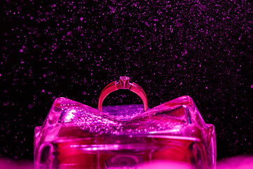 Engagement ring on a violet glass stand with effect of small splashes of water