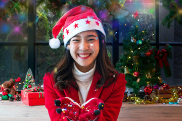Beautiful Asian girl in christmas wearing and santa hat, with two hand holding or offering something, multi colored confetti flying