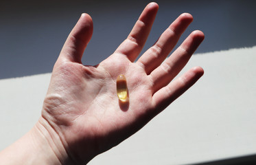 Vitamin D or omega 3 capsules. Vitamin gel in hand against the window. The concept of a lack of vitamin D in the body