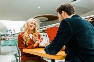 happy attractive woman showing bag with sale tag to boyfriend in shopping mall