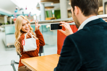 man taking photo of happy beautiful girlfriend holding bag with sale tag