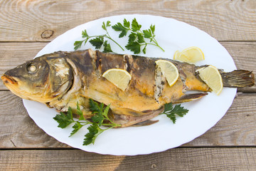 Tasty baked carp in white plate on wooden table. Top view